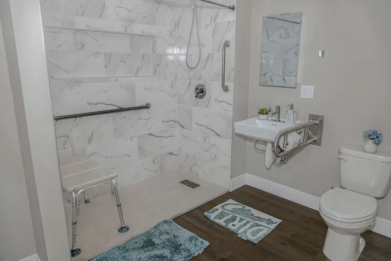 Accessible bathroom with a barrier-free roll-in shower, grab bars, a shower chair and a wall-mounted sink