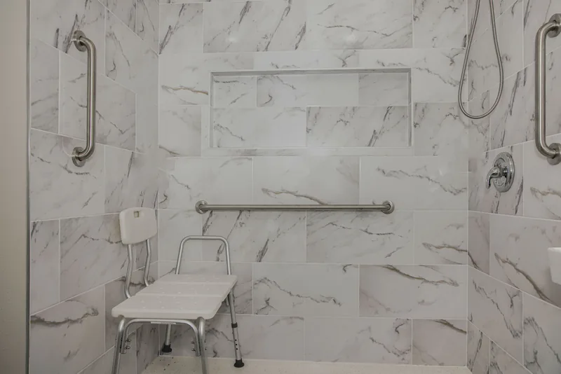 Roll-in shower with marble-look tile, a wall niche, grab bars and a shower seat