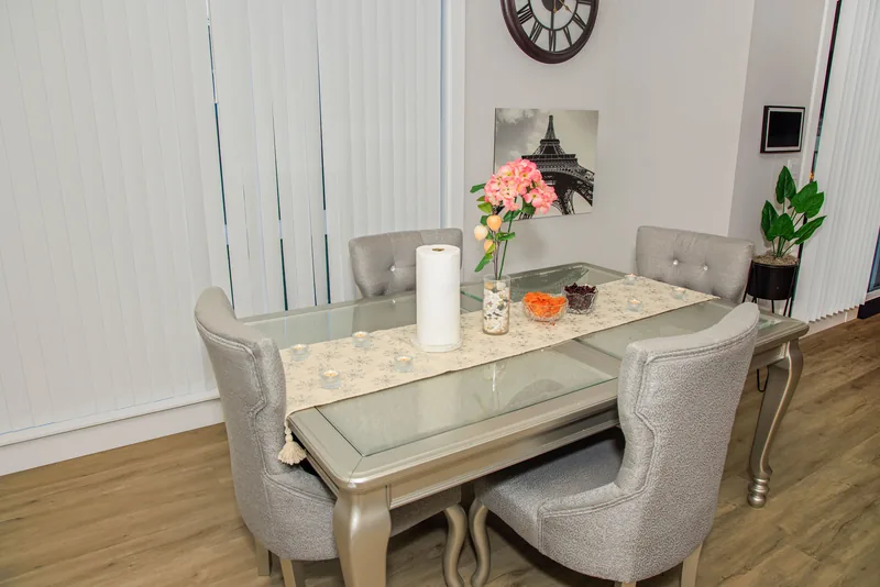 Dining table dressed with a white runner and a floral centerpiece in front of tall windows