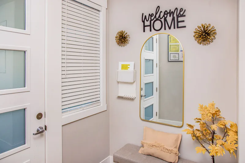 Entry with a 'welcome HOME' sign, a gold-framed arched mirror and a cushioned bench beside the front door
