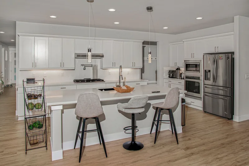 Kitchen island with a deep sink and three cushioned barstools, with a double wall oven and refrigerator behind