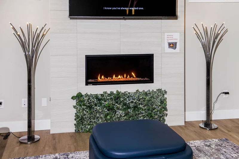 Fireplace feature wall with a glowing electric fireplace, a wall-mounted TV and two slender metallic floor lamps