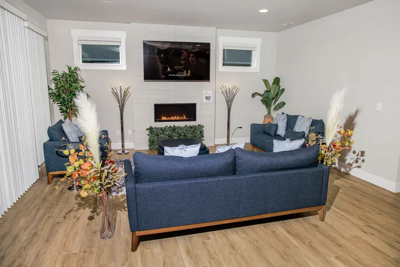 Living room with navy sofas and armchairs around a patterned rug and ottoman, facing a fireplace wall with a wall-mounted TV