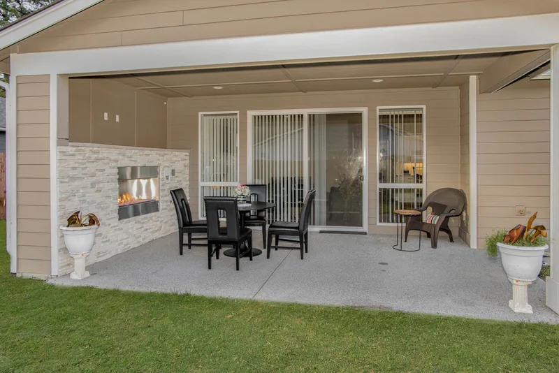 Covered back patio with a round black dining table, four chairs, and a built-in fireplace in a light stacked-stone wall