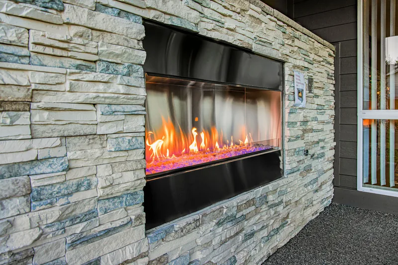 Close view of a linear gas fireplace with orange flames set into a light stacked-stone wall