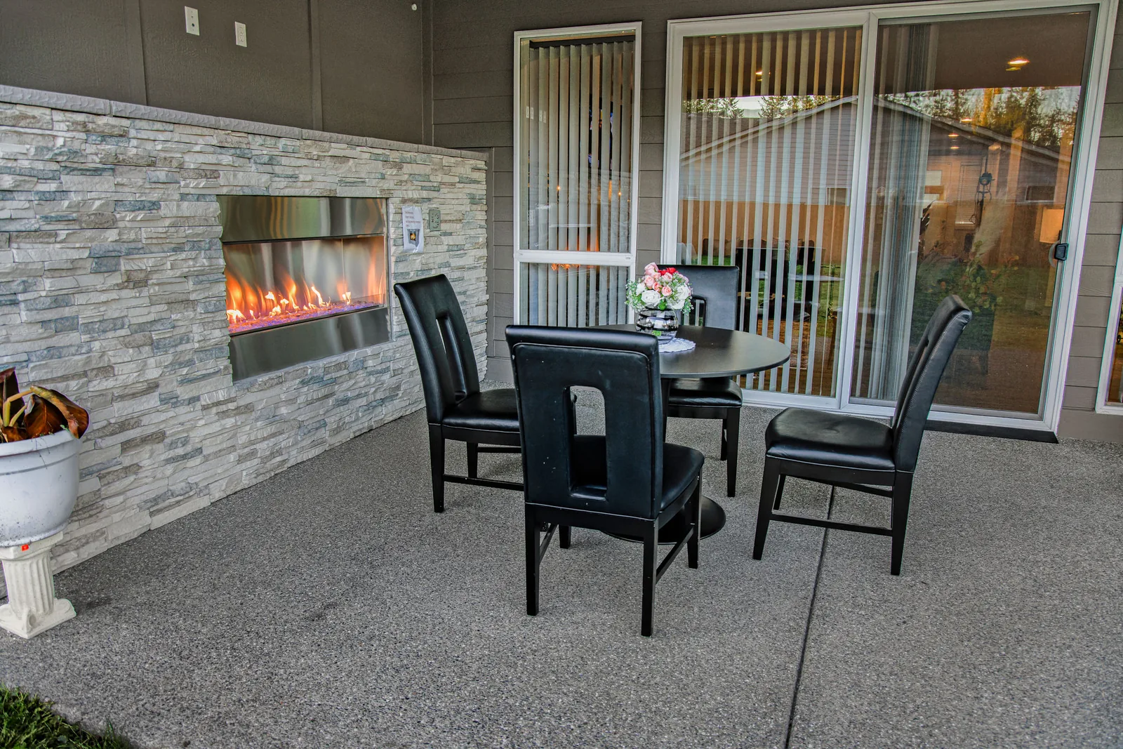 Round black patio table and chairs beside the stone fireplace wall, with glass doors leading back into the home