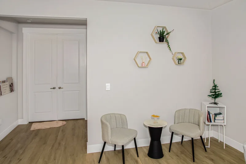 Quiet seating corner with two gray armchairs, a small round table and hexagonal wall shelves holding plants